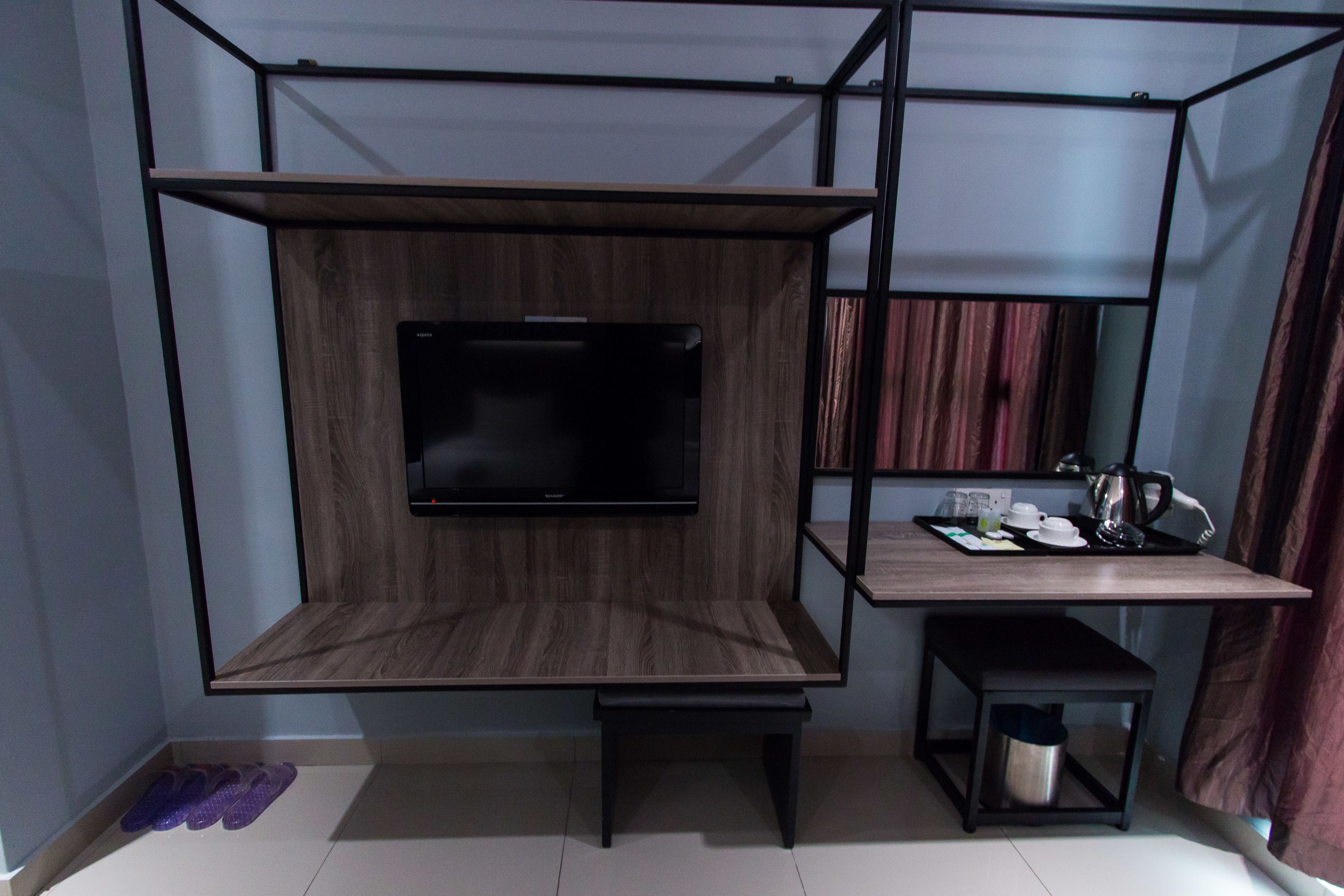 A compact room with a TV mounted on a wooden wall, a small table with a kettle, and a bench.