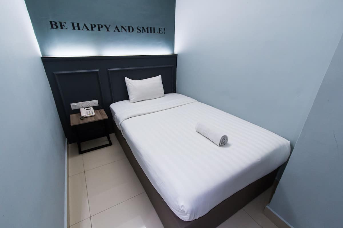Una cama bien tendida en una habitación de hotel, con un cabecero, una mesita de noche con un teléfono y una pared con una cita motivacional.
