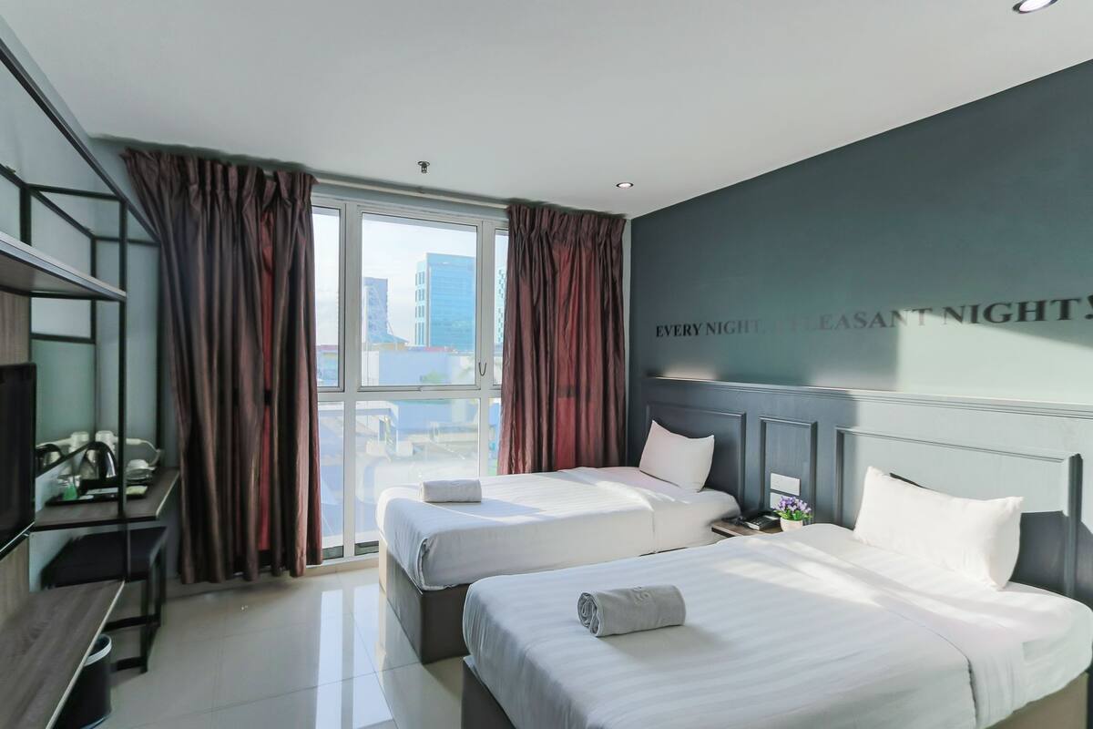 Habitación de hotel con dos camas, un escritorio y un ventanal grande con cortinas.