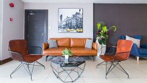 Eine moderne Lobby mit einem braunen Ledersofa, zwei Metallstühlen, einem Marmortisch mit Pflanze und einem Stadtbild an der Wand.