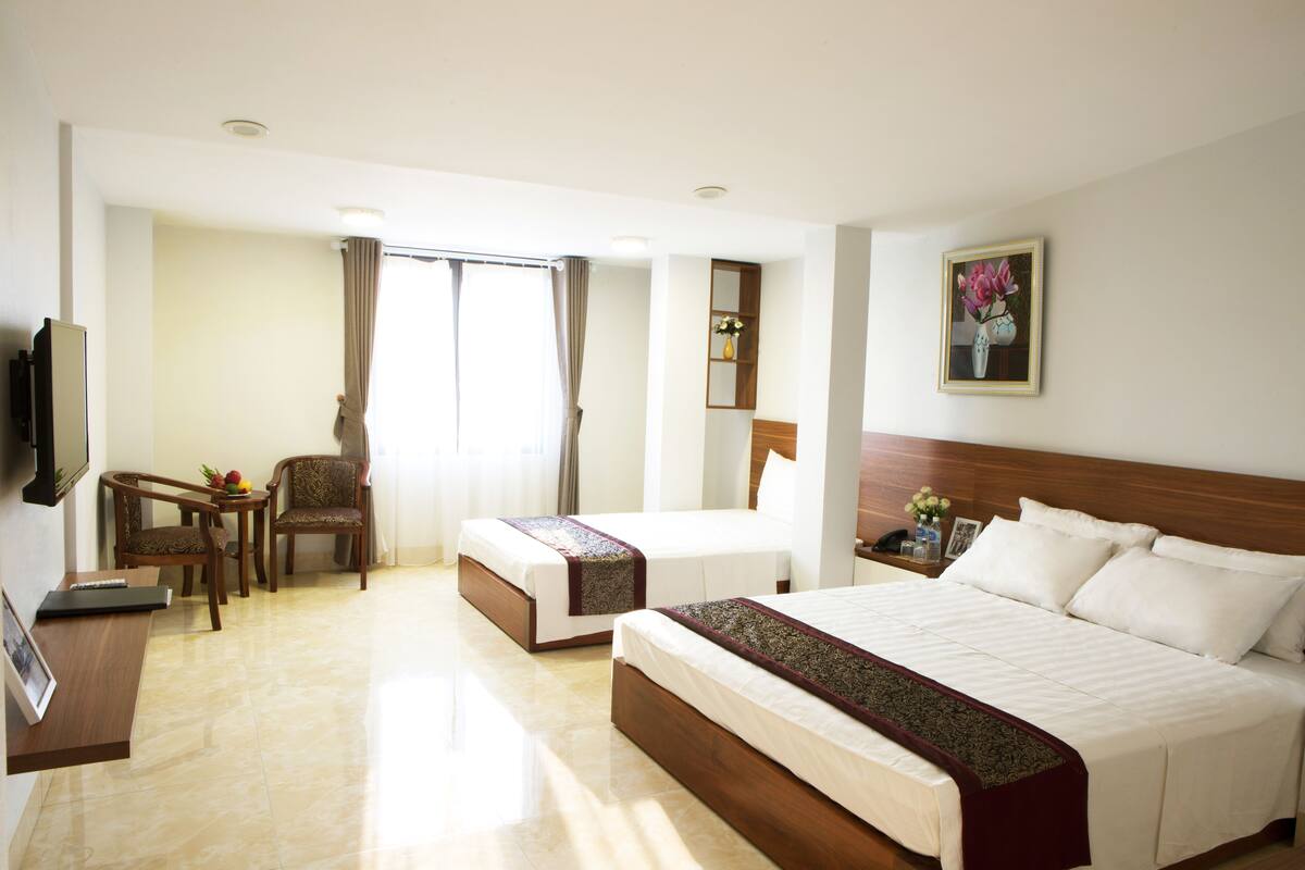 A hotel room with two beds, a desk, a chair, a television, and a window with curtains.