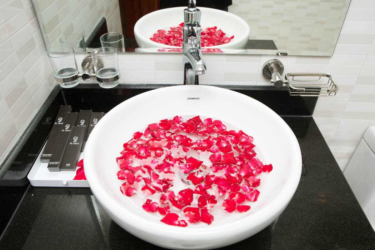 A bathroom sink with rose petals in the bowl, a mirror above, and a towel rack to the right.