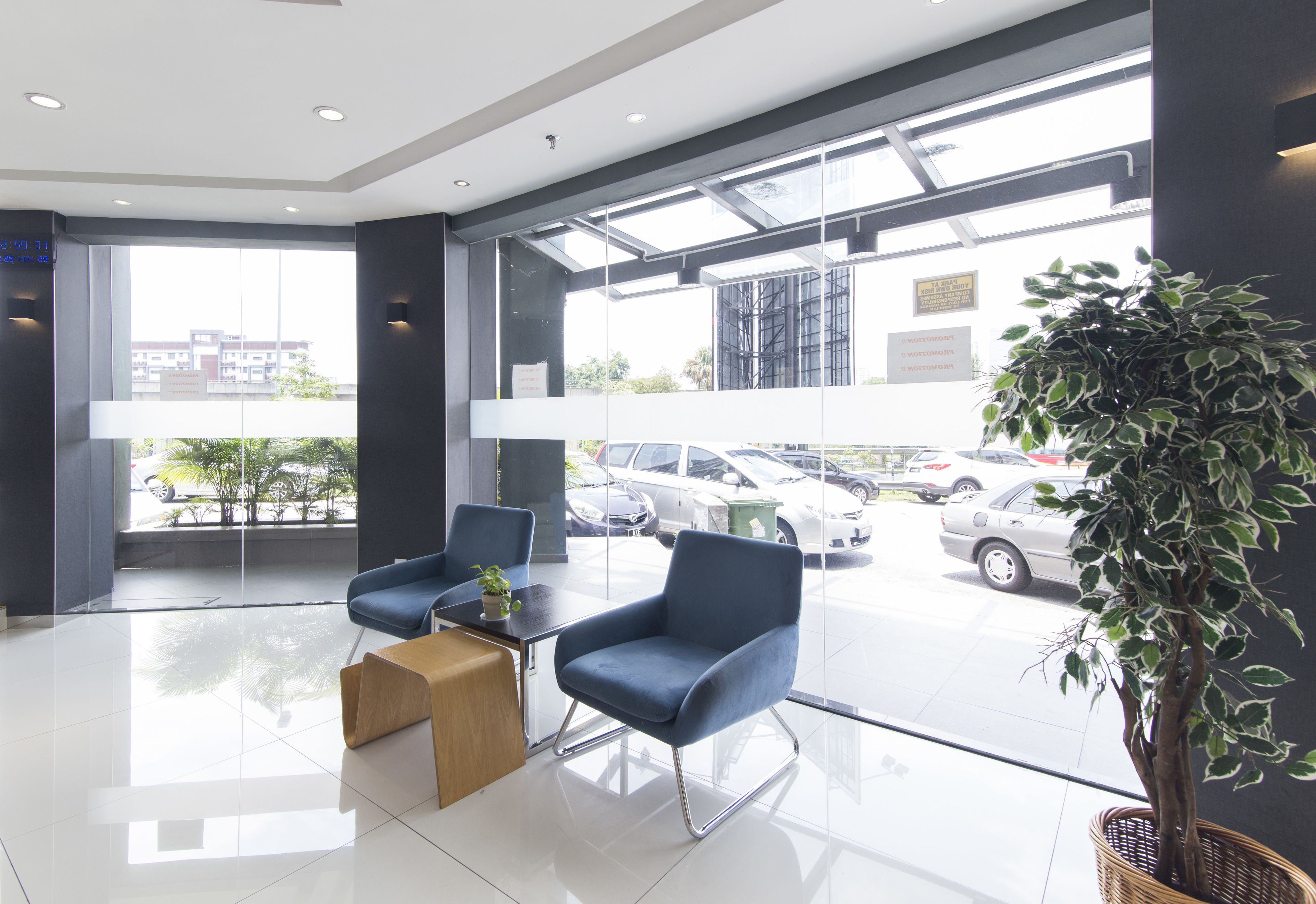 A modern lobby with glass walls, two blue armchairs, a wooden coffee table, and a potted plant.