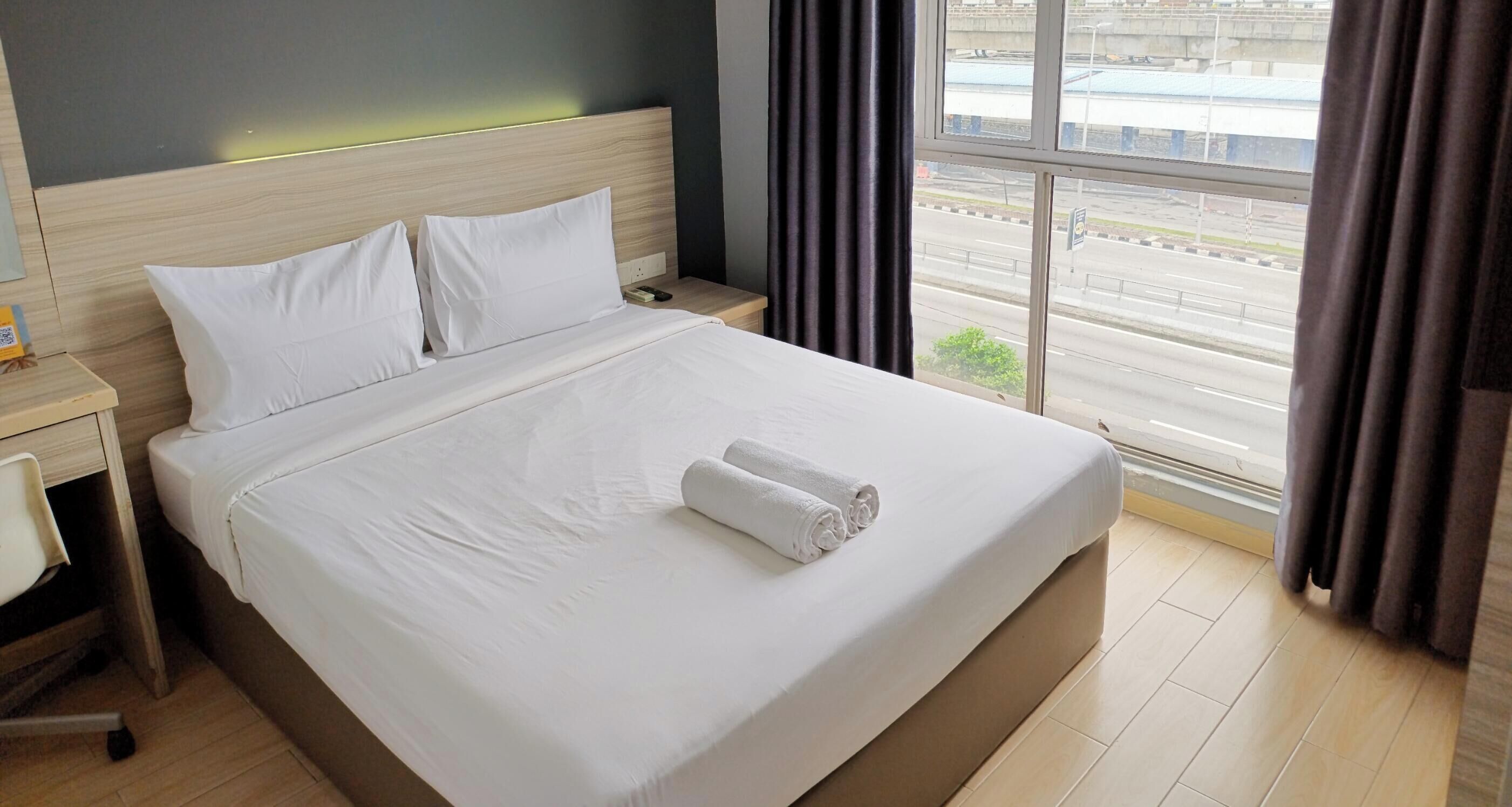 Habitación de hotel con una cama grande, una mesita de noche, una silla y una ventana con vista a la calle.