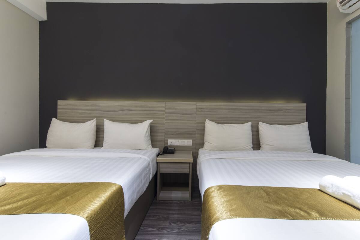 Habitación de hotel con dos camas, una mesita de noche y un cabecero moderno.