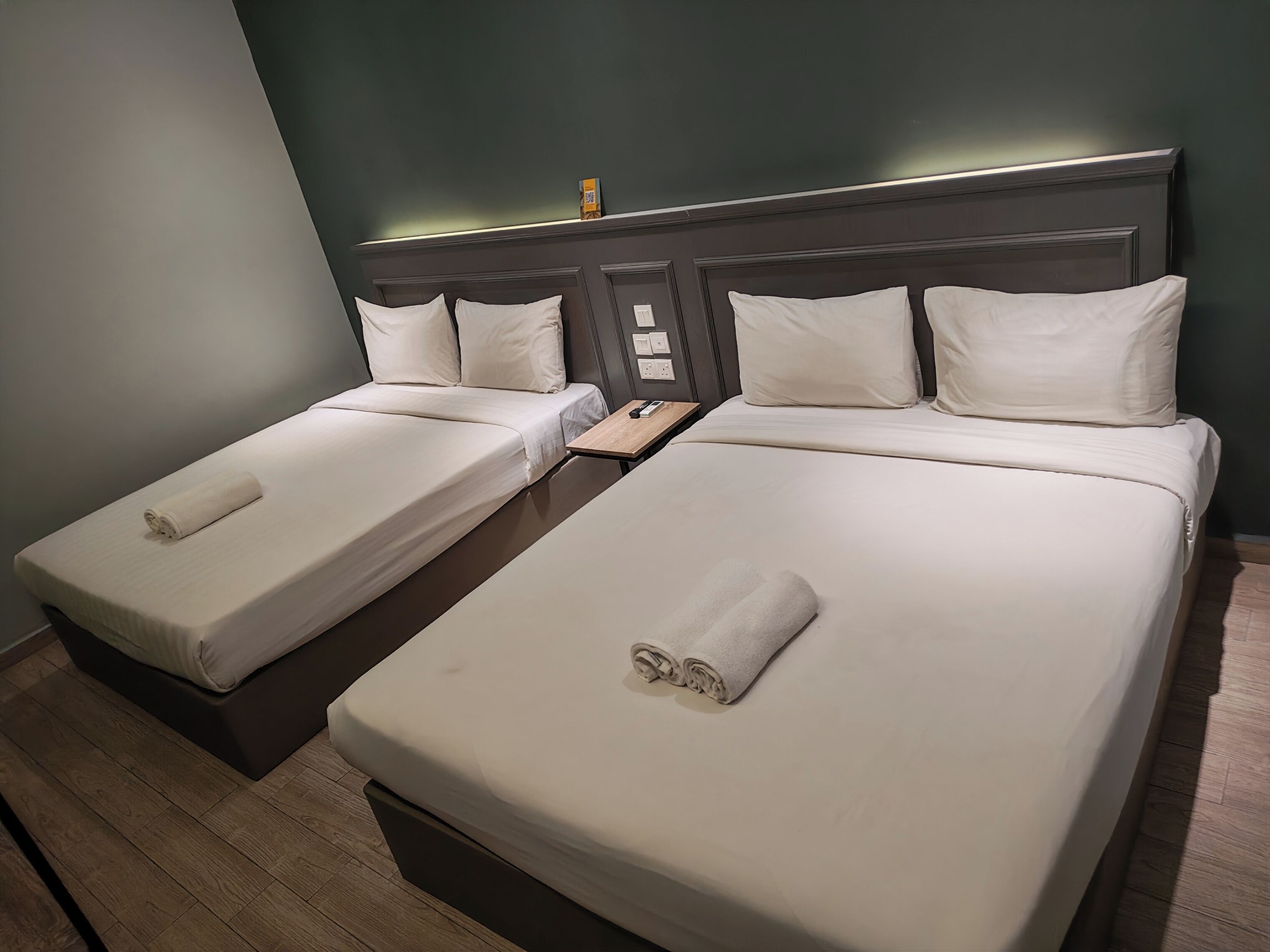 A hotel room with two single beds, a wooden nightstand, and a headboard with built-in lighting.