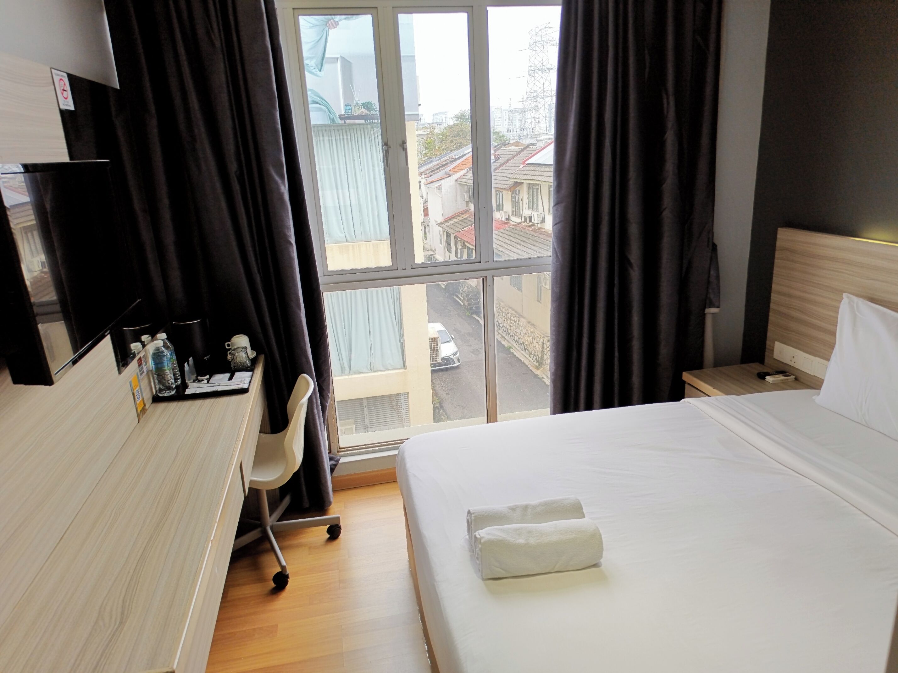 A hotel room with a bed, a desk, a chair, and a window with a view of buildings.