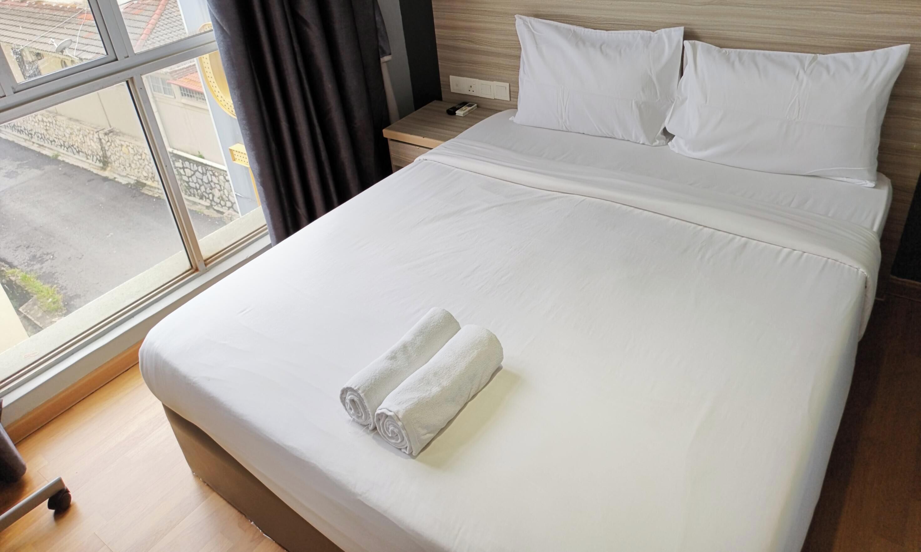 A hotel room with a bed, a nightstand, a window, and a view of the street.