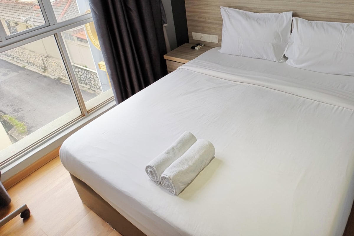 A hotel room with a bed, a nightstand, a window, and a view of the street.