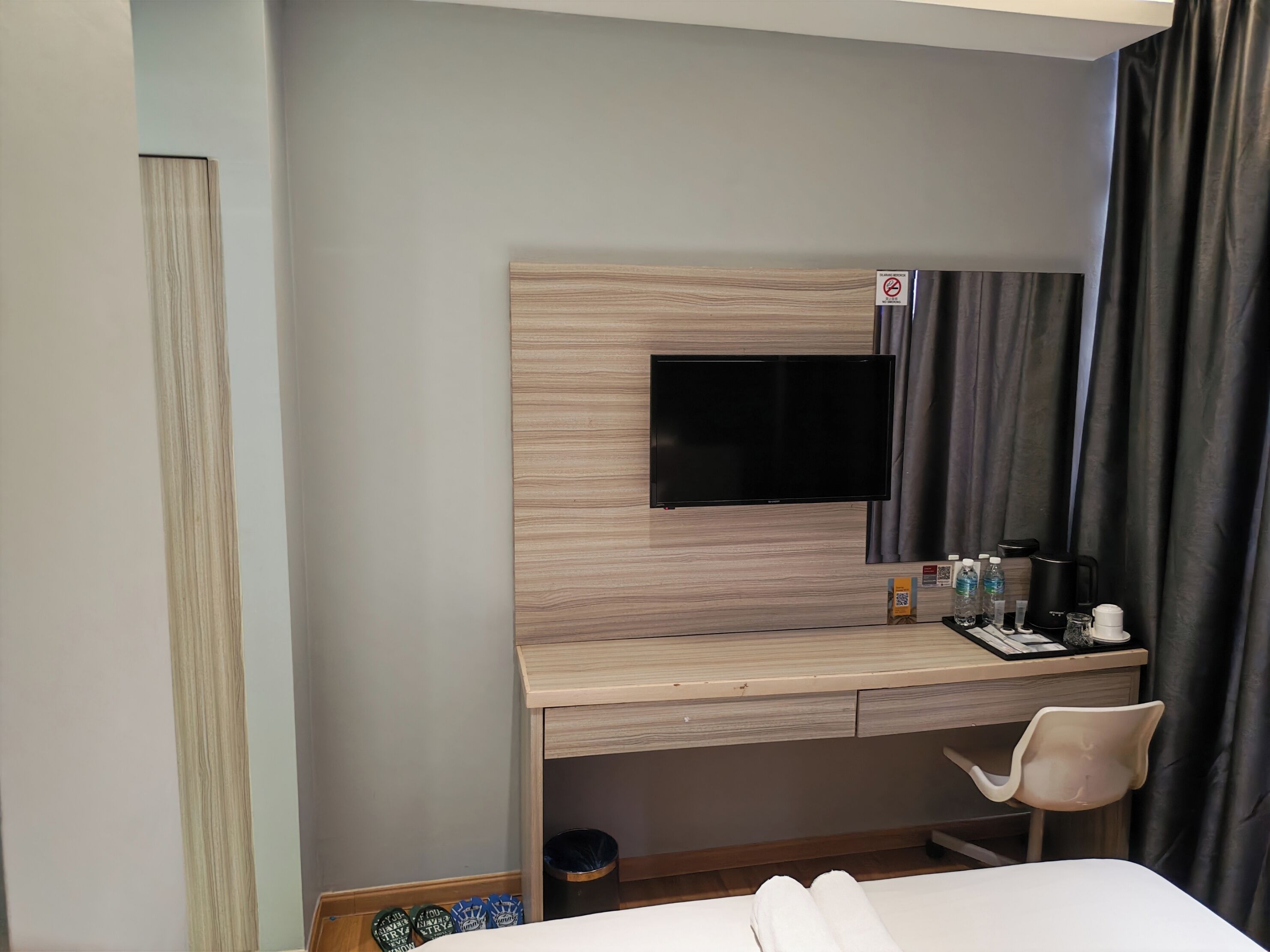 Habitación de hotel con cama, escritorio con televisor de pantalla plana, silla, pequeño cubo de basura y minibar.
