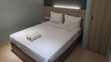 A neatly made bed with a white duvet and a rolled towel, a wooden headboard, and a nightstand with a phone.