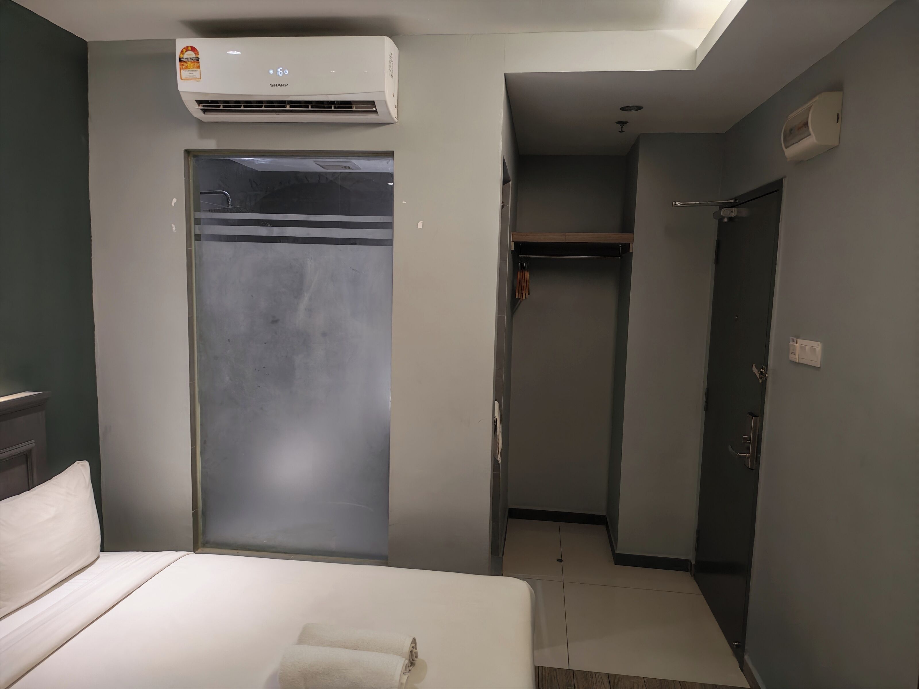 A hotel room with a bed, a wardrobe, a closet, and an air conditioning unit.