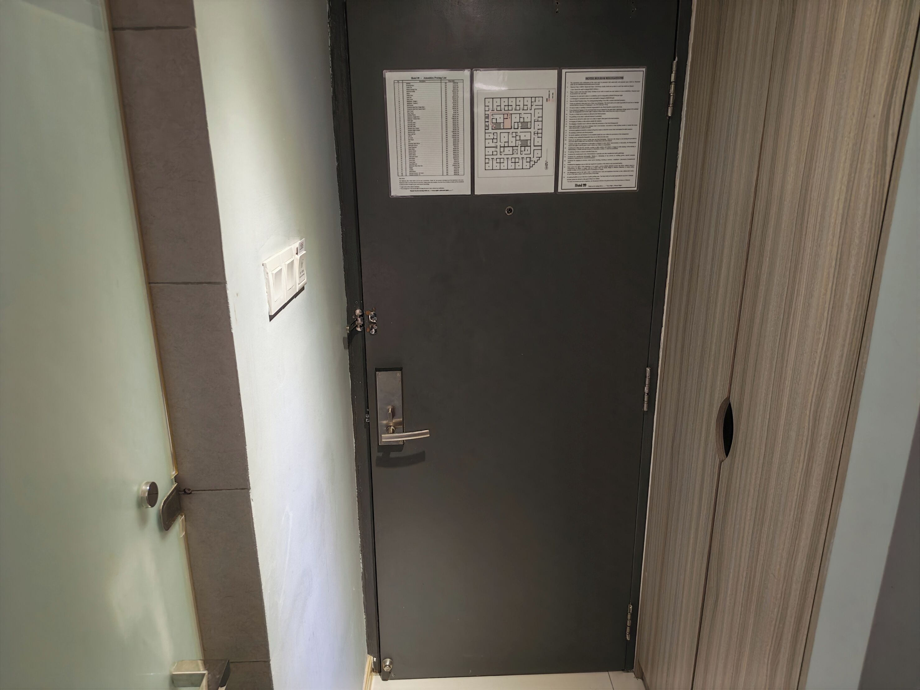 A closed door with a metal handle and a keyhole, a light switch, and two informational posters on the wall.
