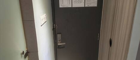 A closed door with a metal handle and a keyhole, a light switch, and two informational posters on the wall.