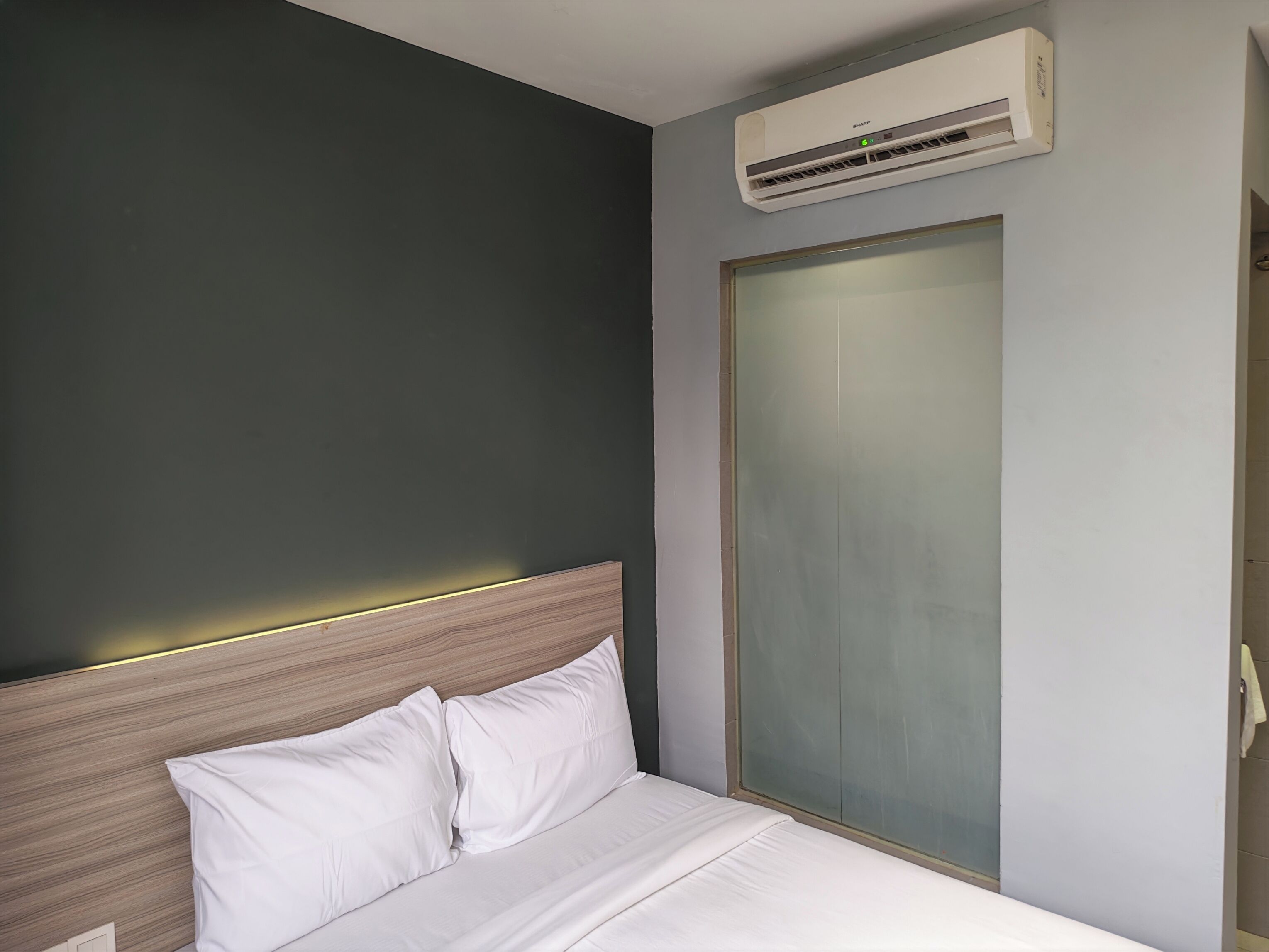 A hotel room with a bed, a wall-mounted air conditioner, and a sliding door closet.
