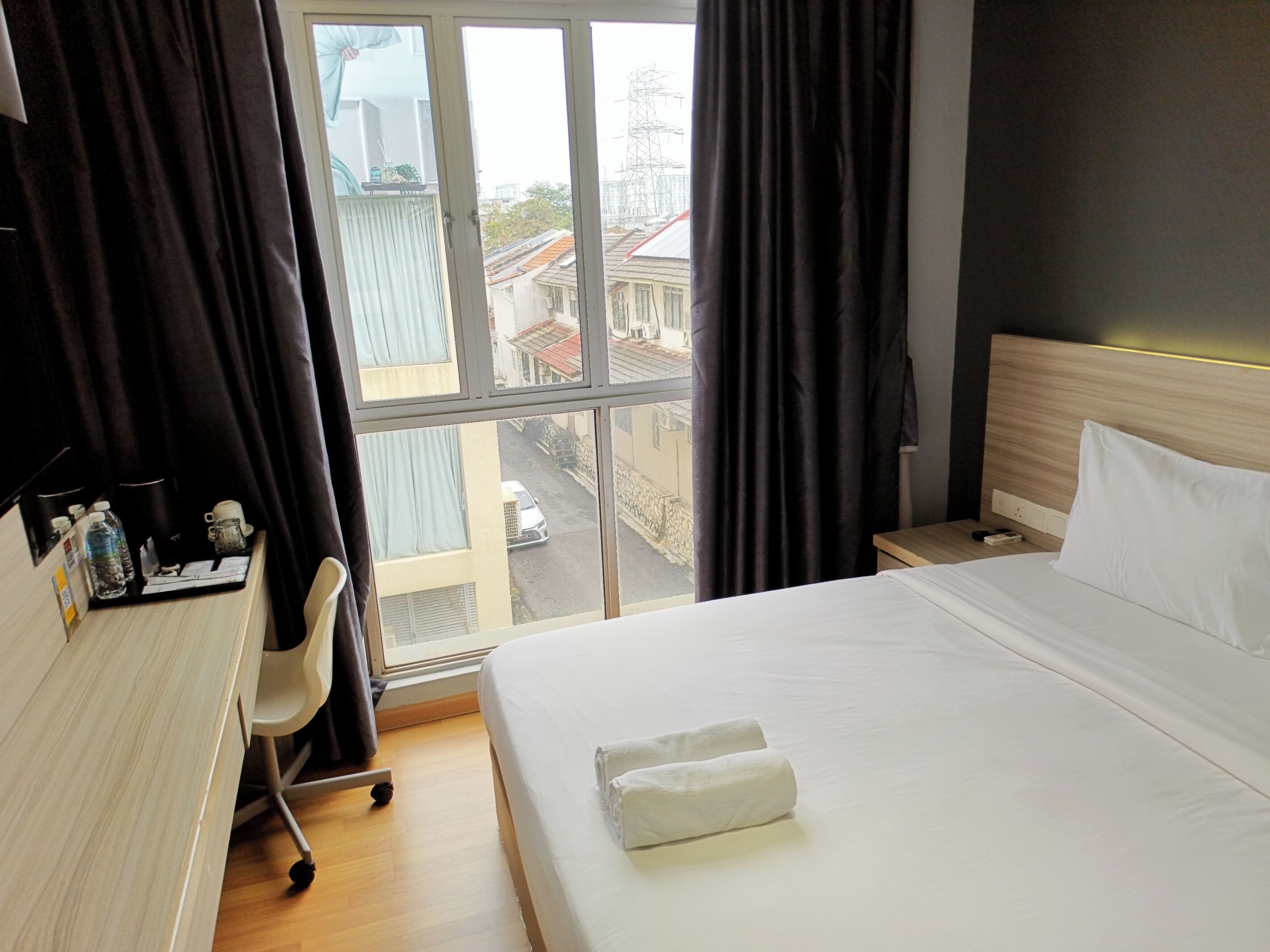 Habitación de hotel con cama, escritorio, silla y vista a la calle a través de una ventana.