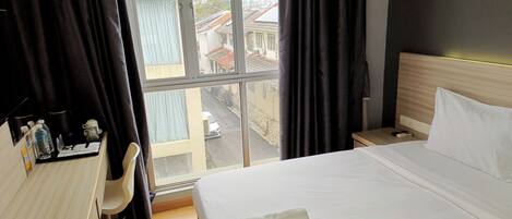 Habitación de hotel con cama, escritorio, silla y vista a la calle a través de una ventana.
