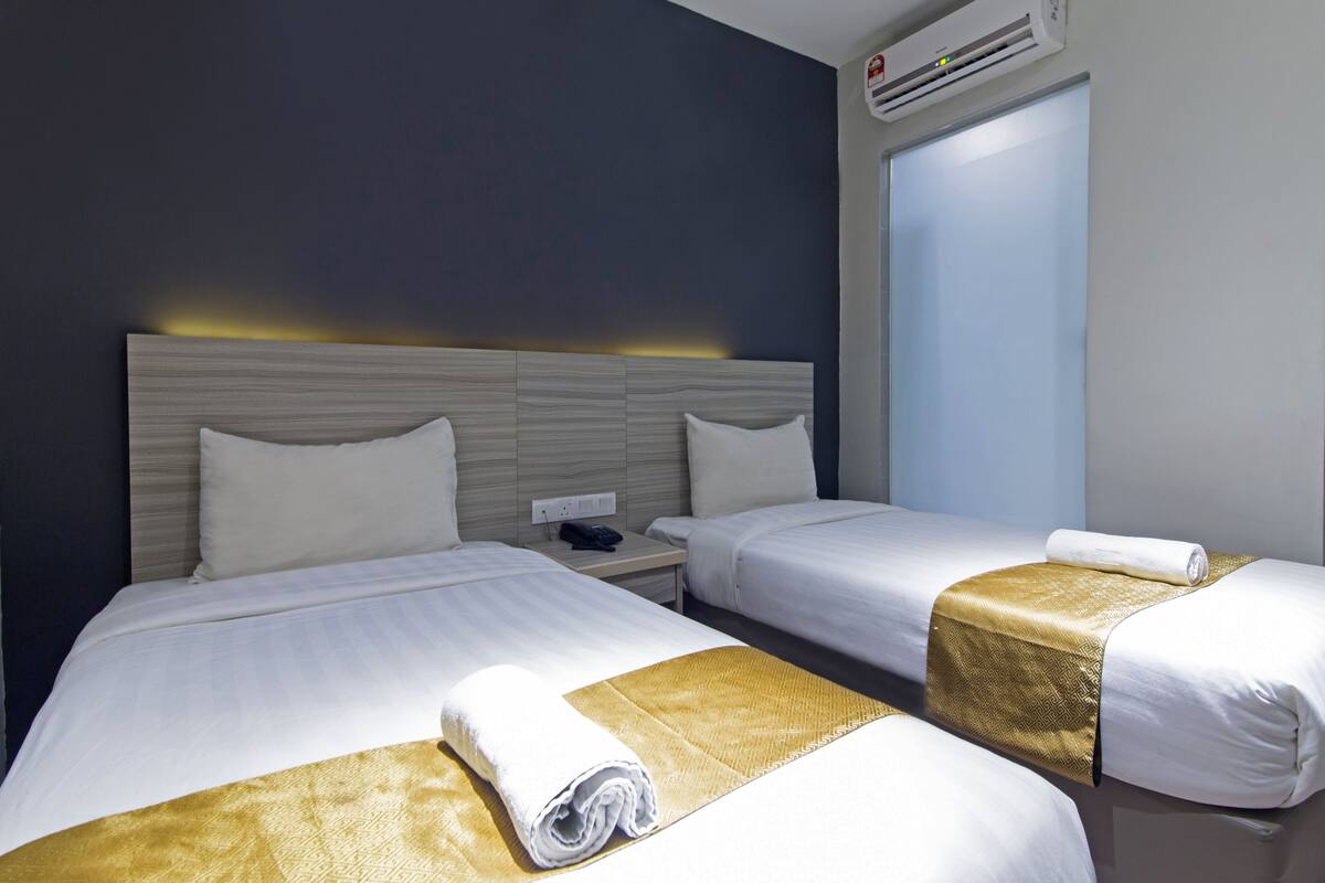Habitación de hotel con dos camas, una mesita de noche, teléfono y aire acondicionado.