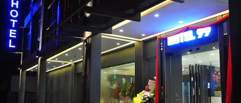 A modern hotel entrance with a glass facade, a red carpet, and a flower arrangement outside.