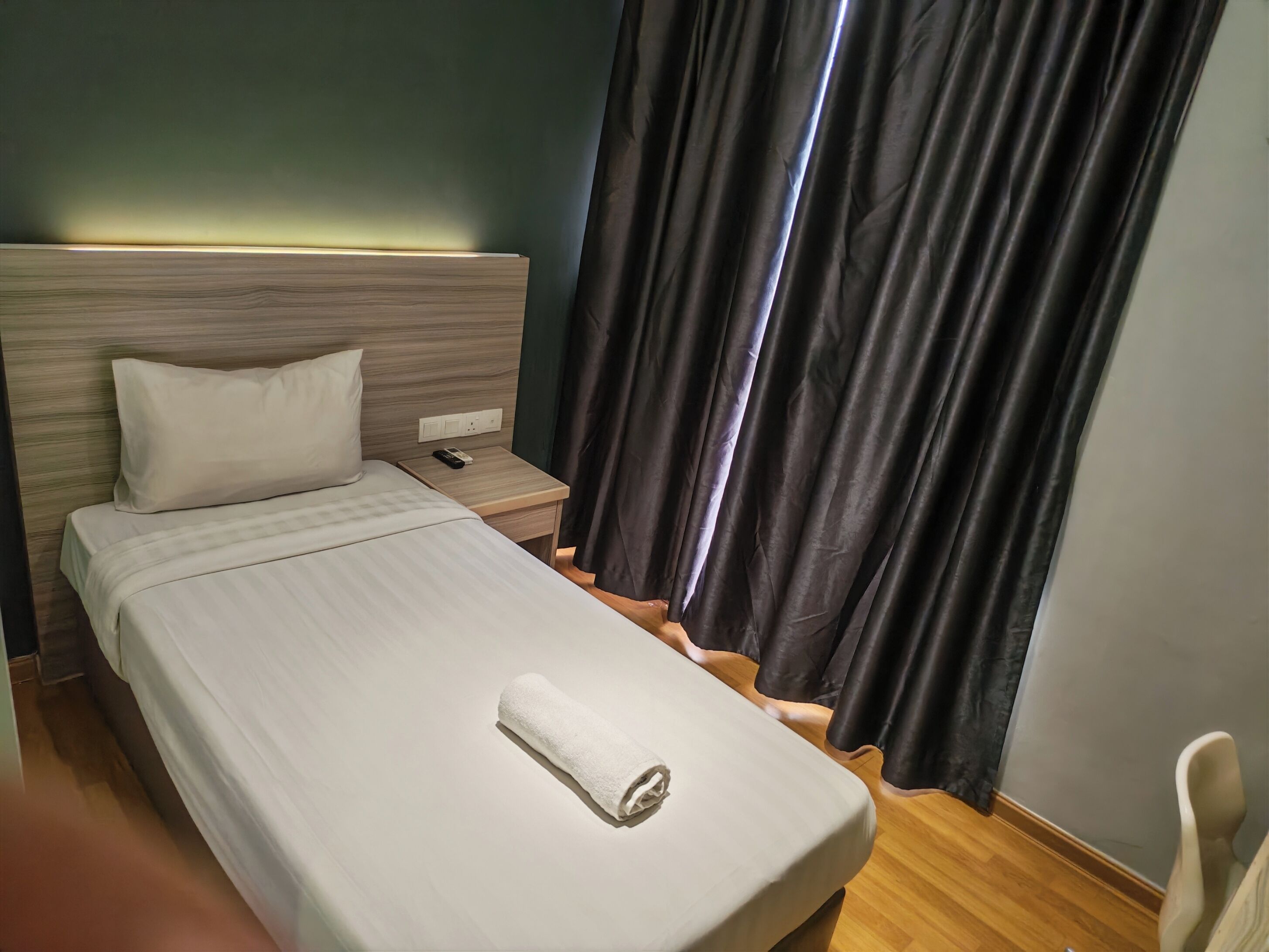 A hotel room with a bed, a nightstand, a remote control, a towel, and a chair.