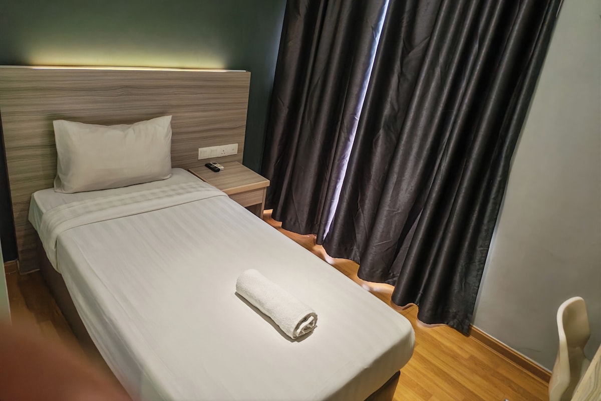 A hotel room with a bed, a nightstand, a remote control, a towel, and a chair.