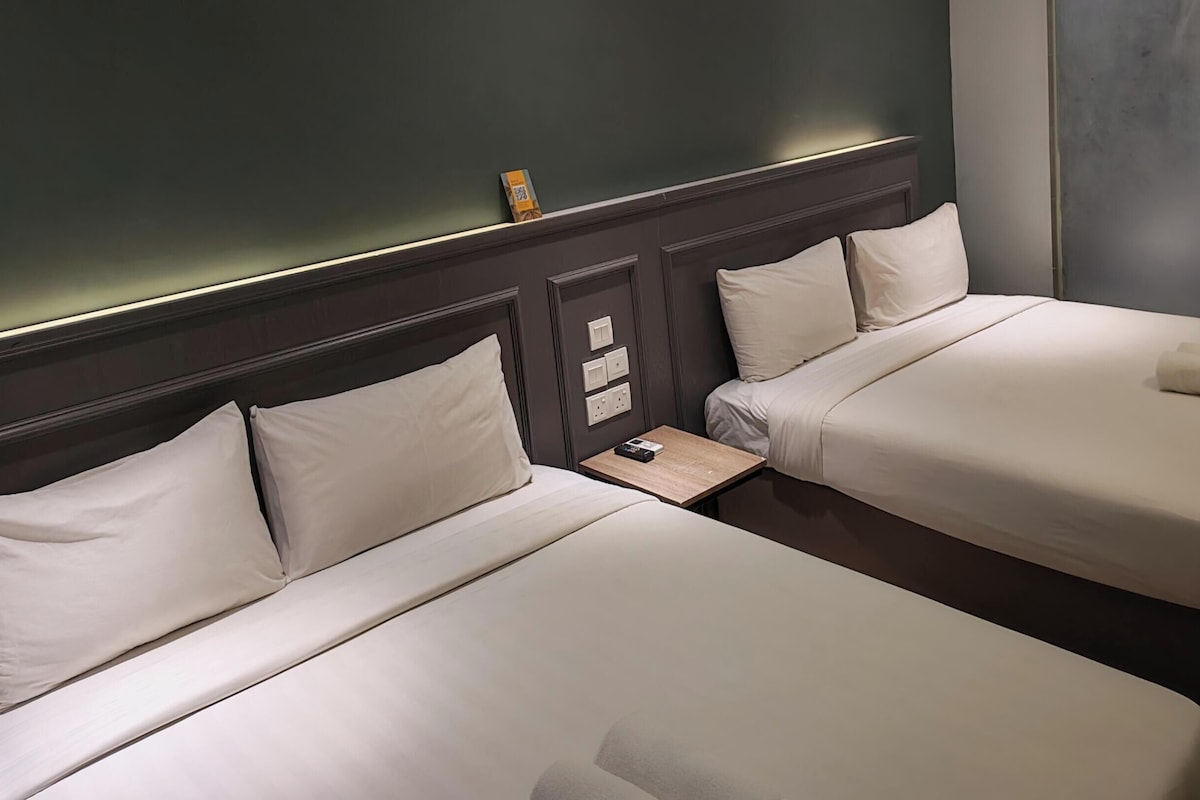 Two single beds with white linens, a nightstand with a remote control, and a wall-mounted light fixture.