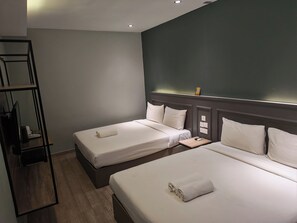 A hotel room with two single beds, a small table, a desk with a chair, and a mirror.