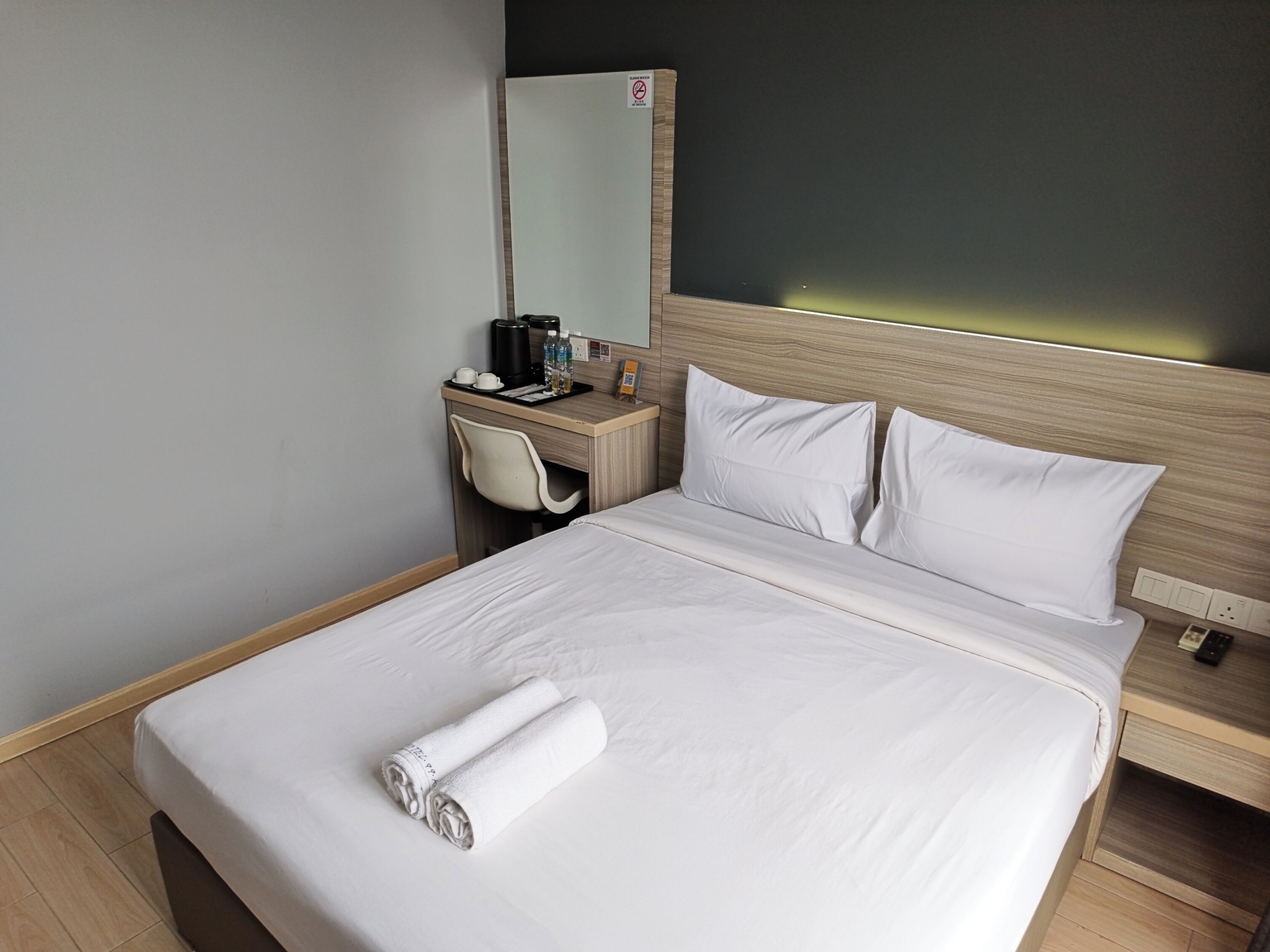 A hotel room with a bed, a desk, a chair, and a mirror.