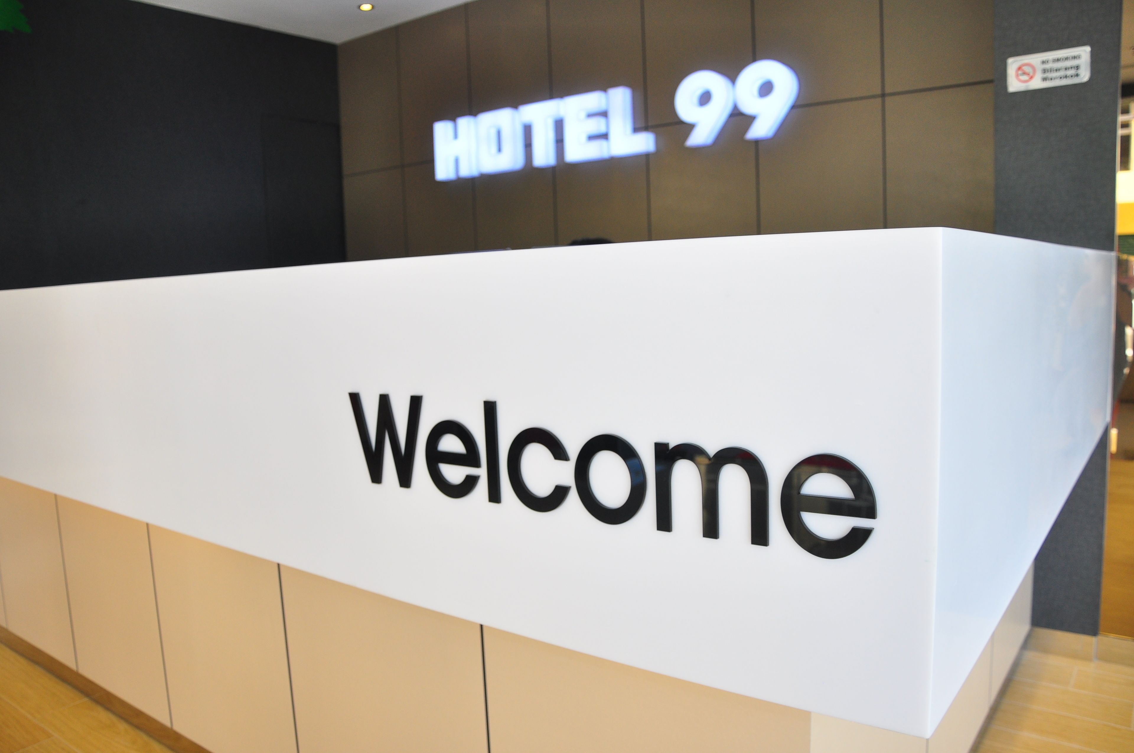 A reception desk with a 'Welcome' sign and a 'HOTEL 99' sign above it.