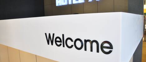 A reception desk with a 'Welcome' sign and a 'HOTEL 99' sign above it.