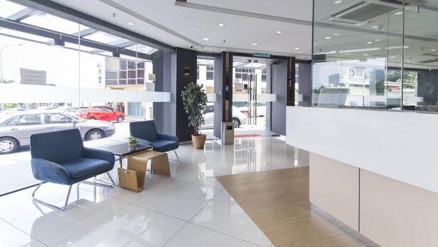 A modern reception area with a glass door, two blue chairs, a wooden table, and a potted plant.