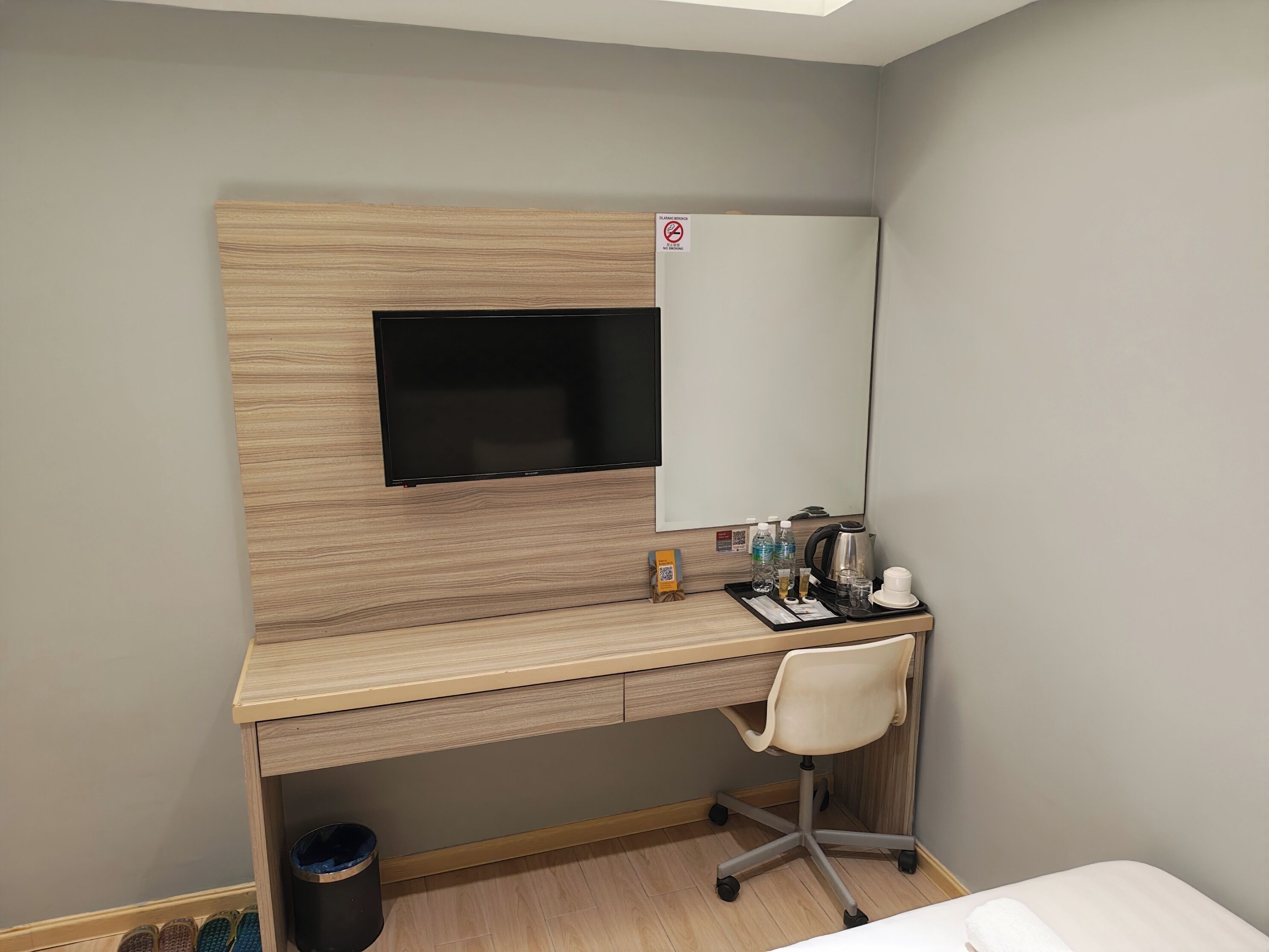 A hotel room with a wooden desk, a TV, a chair, and a small table with toiletries.