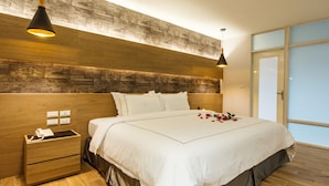 Una habitación de hotel moderna con una cama grande, cabecera de madera y una mesita de noche con teléfono.