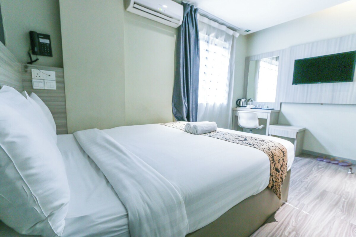 A hotel room with a bed, a desk with a chair, a mirror, an air conditioner, and a telephone.