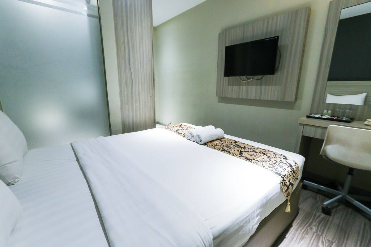 Una camera d'albergo con un letto, una scrivania con una sedia, una televisione e uno specchio.
