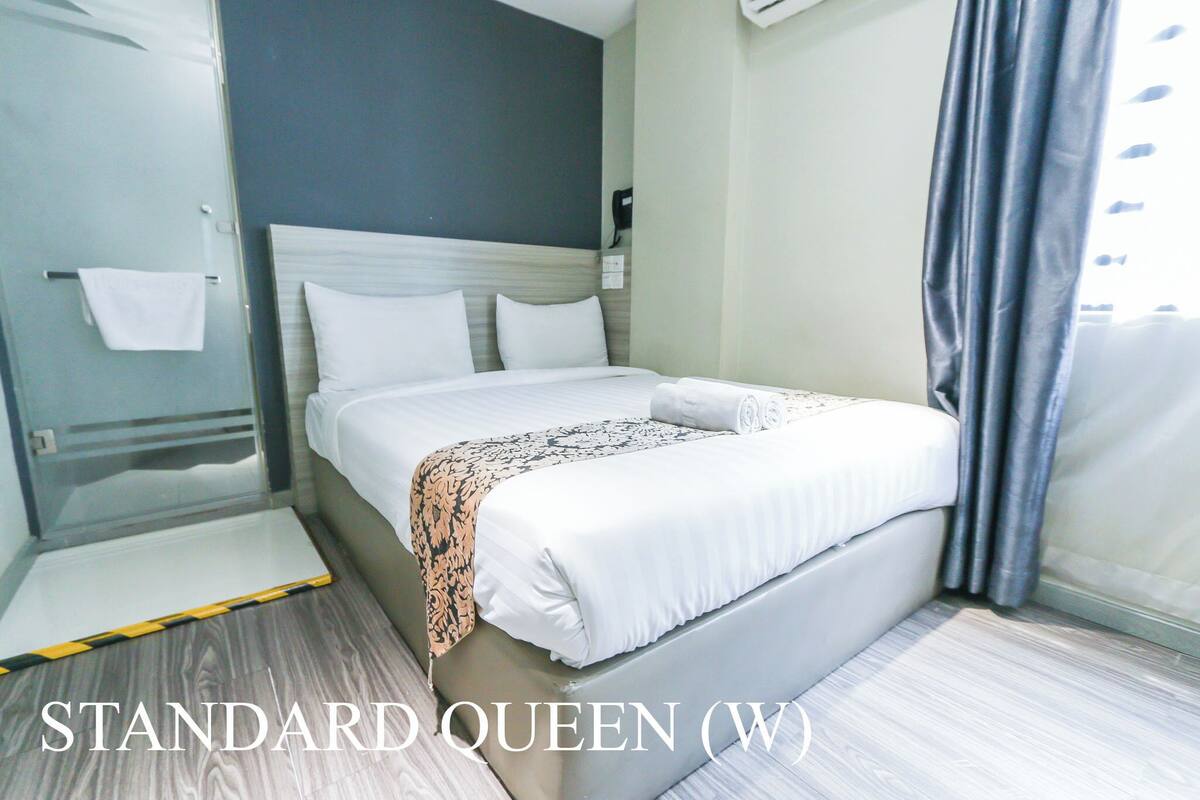 Un letto queen standard con copriletto decorato, un comodino e un asciugamano su un portasciugamani.