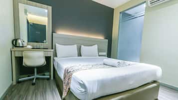 A hotel room with a bed, a desk with a chair, a mirror, and an air conditioning unit.