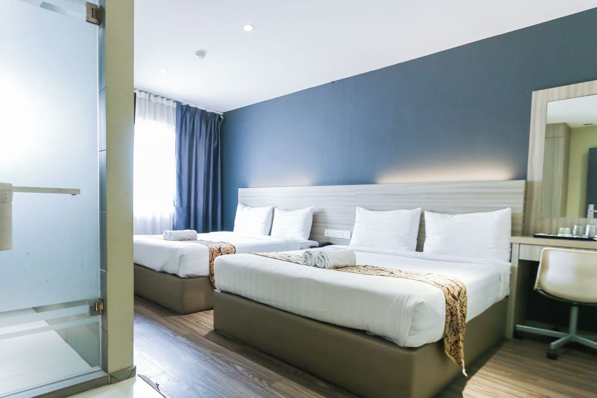 A hotel room with two beds, a desk, and a shower area.