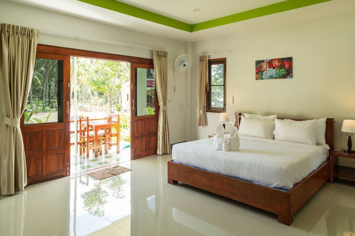 Habitación de hotel con cama de madera, pared de acento verde, un cuadro y vistas al exterior.