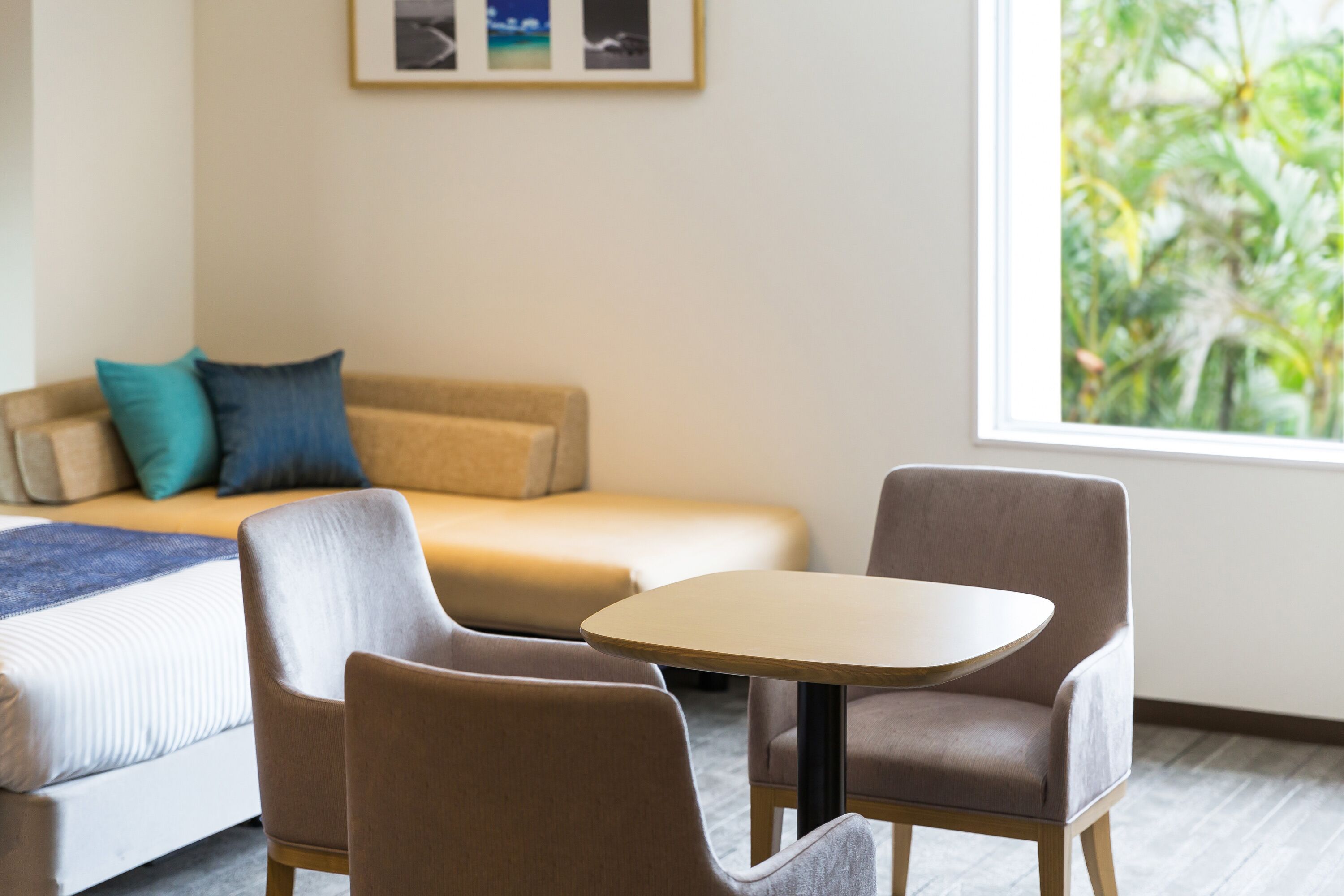 Habitación de hotel moderna con sofá, dos sillones, una mesita redonda y un ventanal con vistas a zonas verdes.