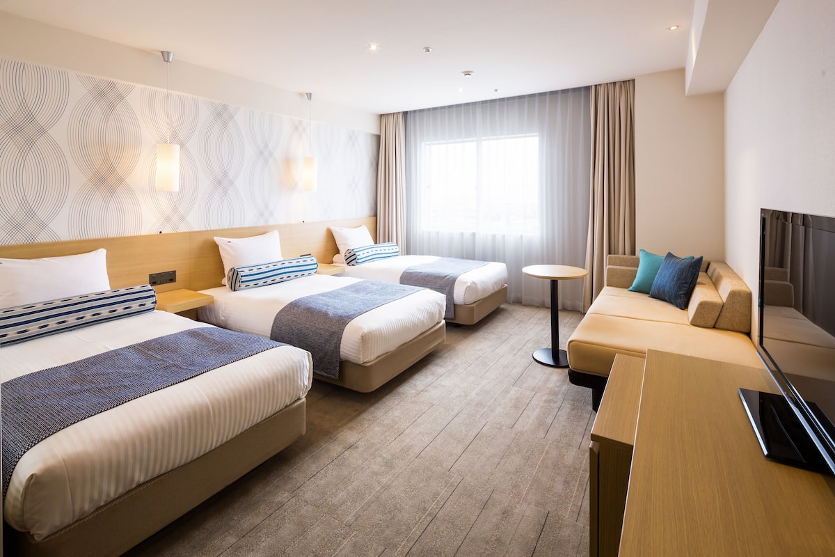 A hotel room with two beds, a sofa, a TV, and a small table.