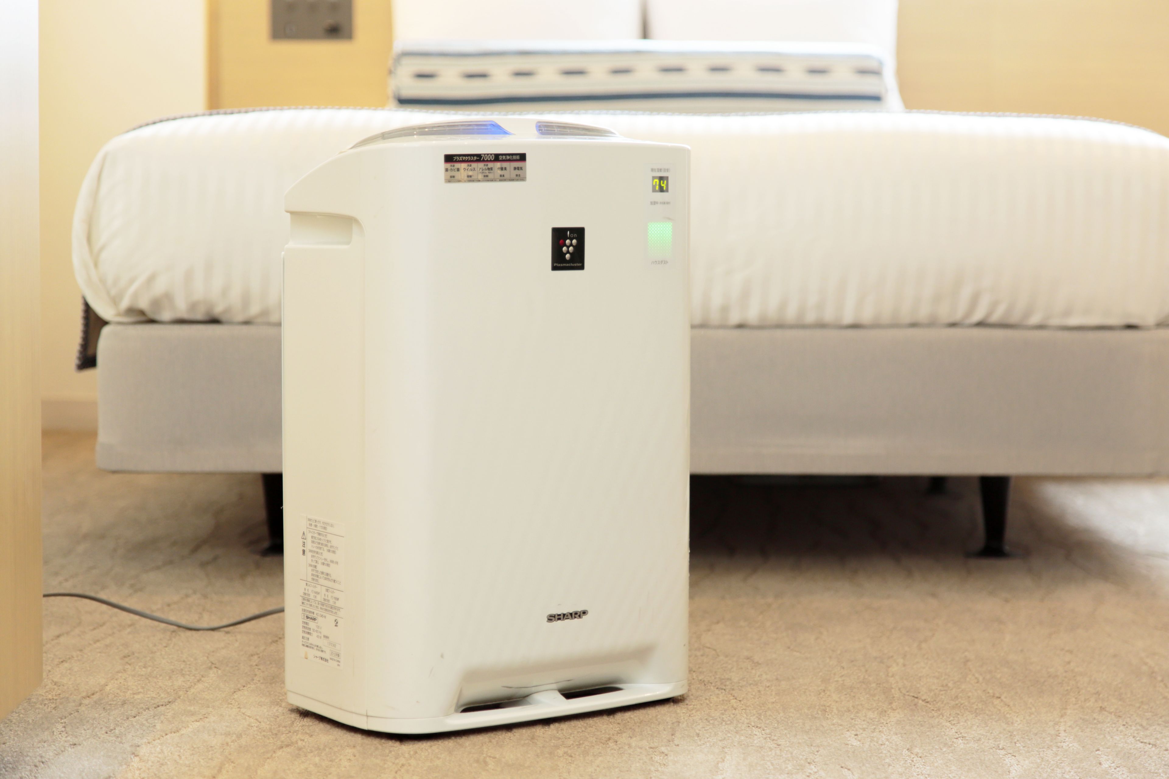 A portable air conditioner in a hotel room with a bed and a bedside table.