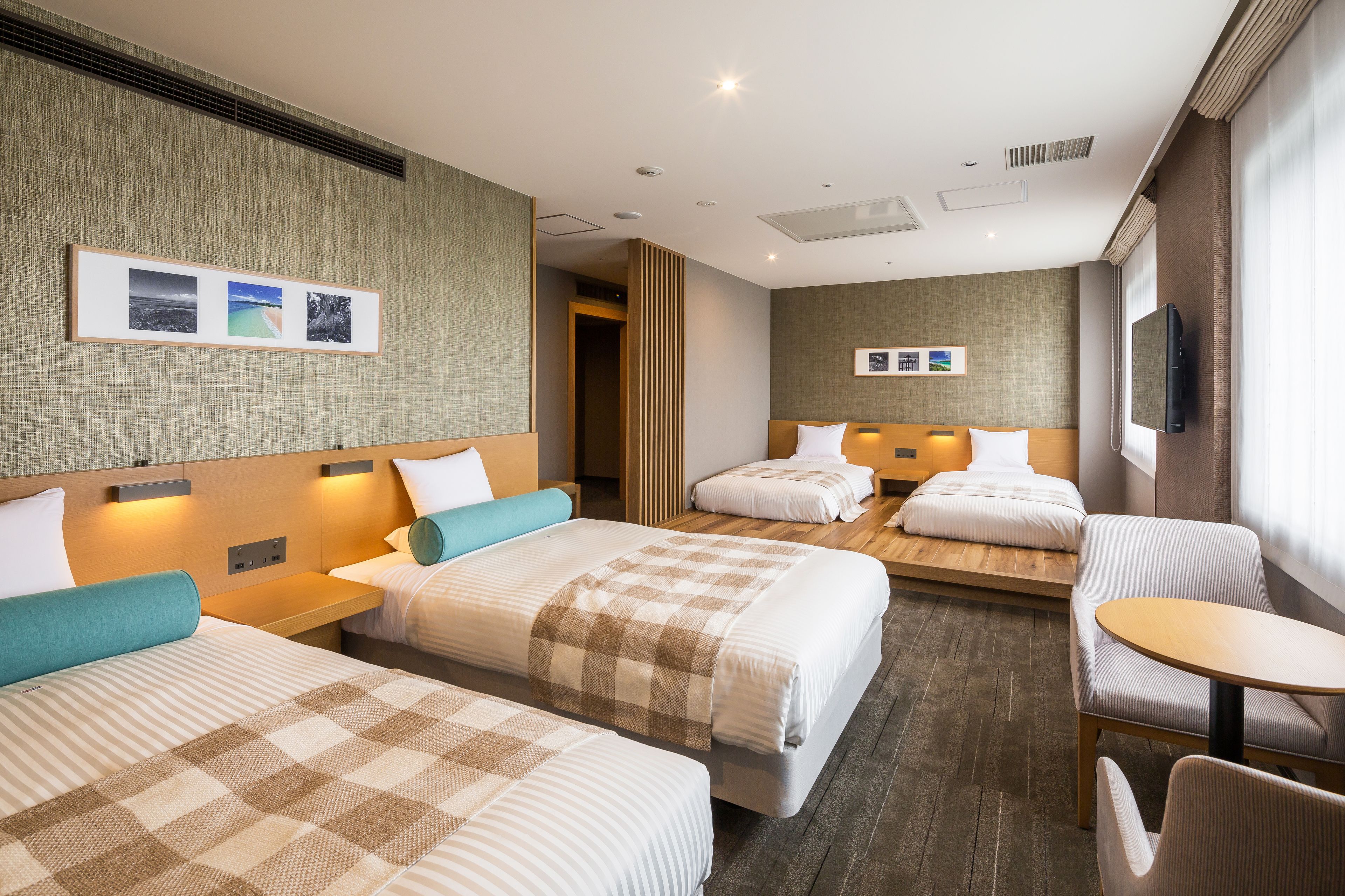 A hotel room with two beds, a sofa, a small table, and a TV.