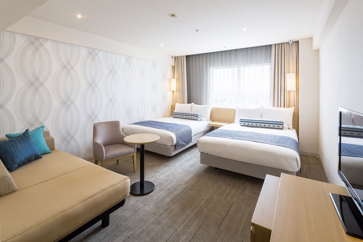 A hotel room with two beds, a sofa, a small table, and a TV.