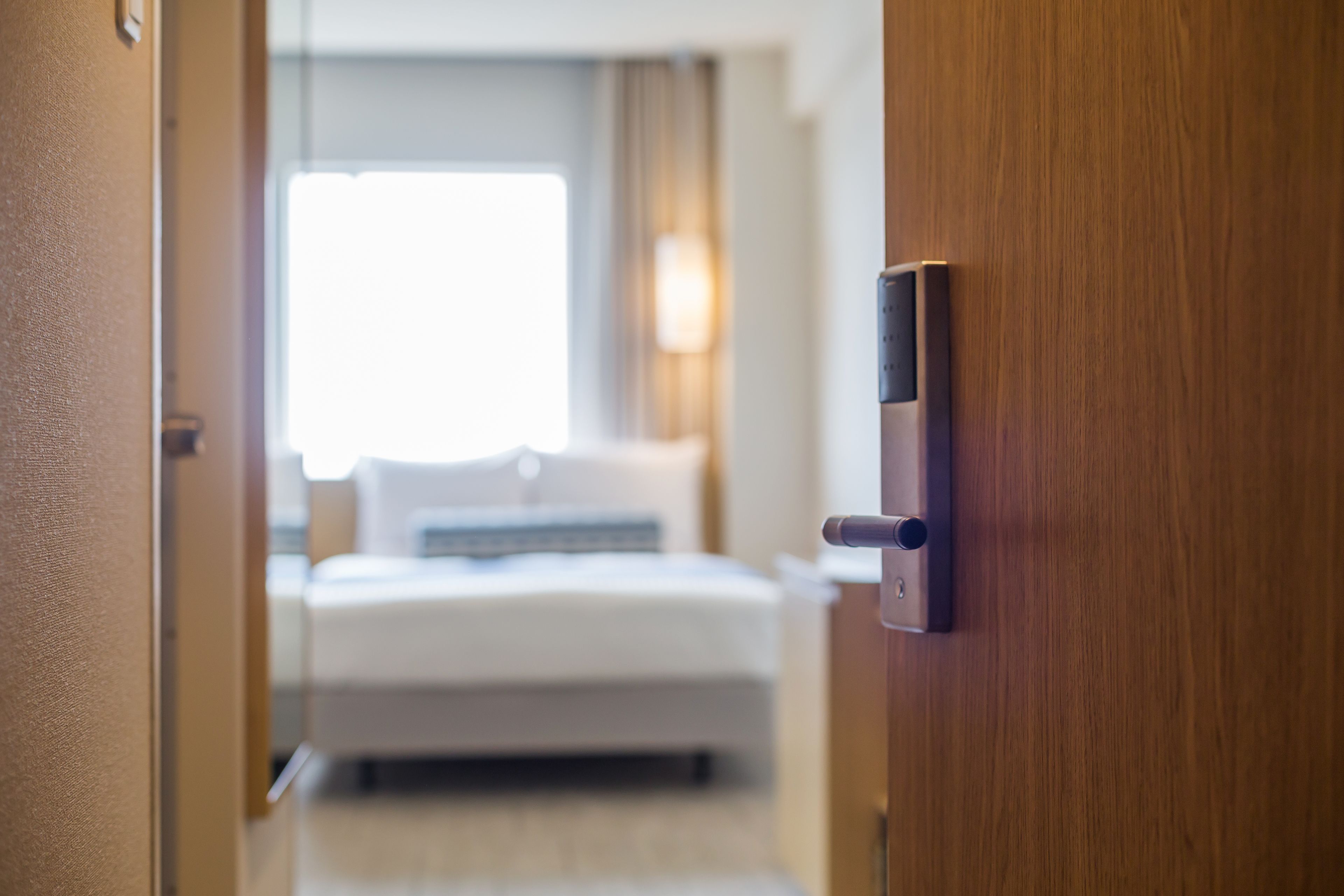 A hotel room with a bed, a bedside table, and a door with a lock.