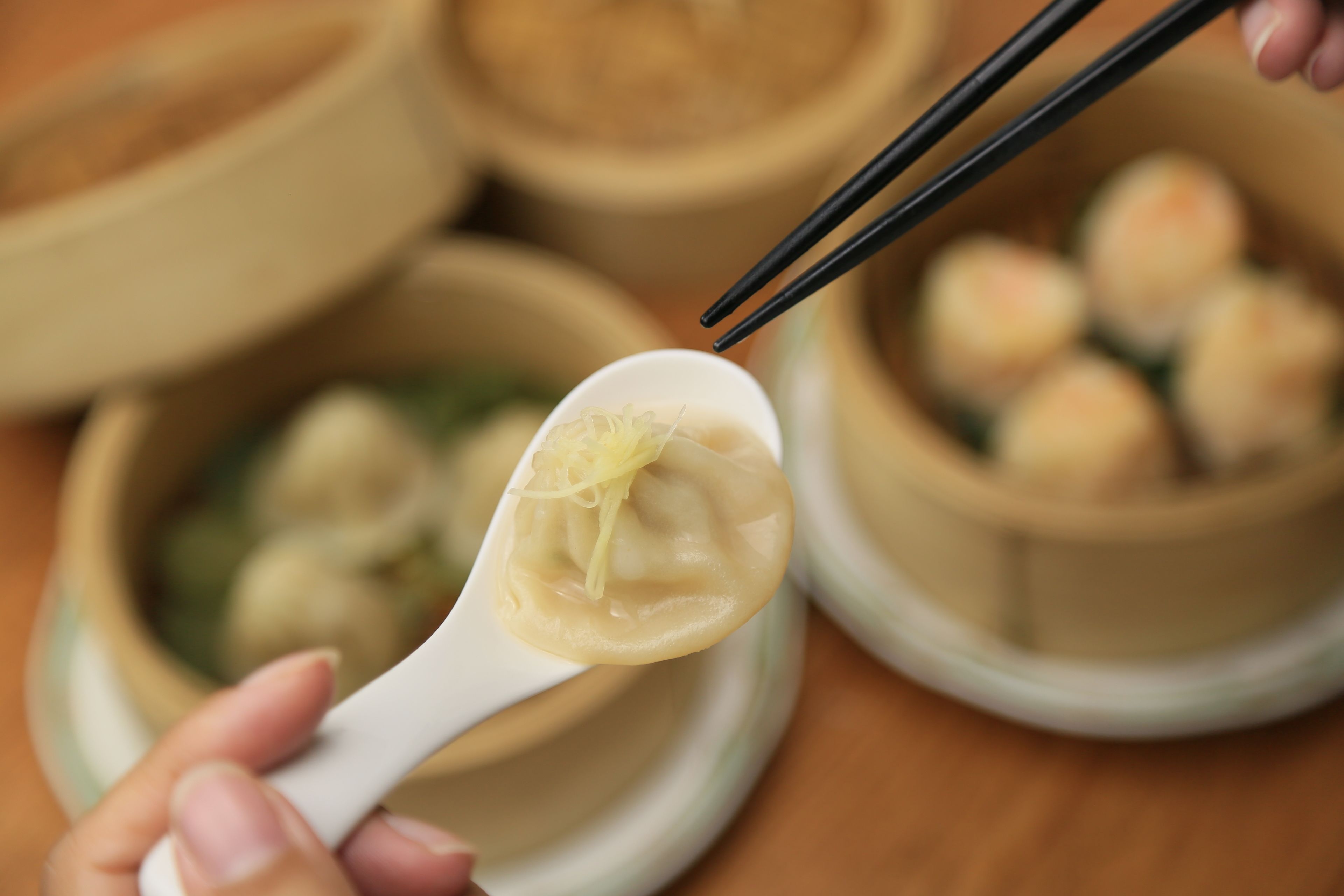 A close-up of a hand holding a spoon with dumplings, with a blurred background of similar food items.