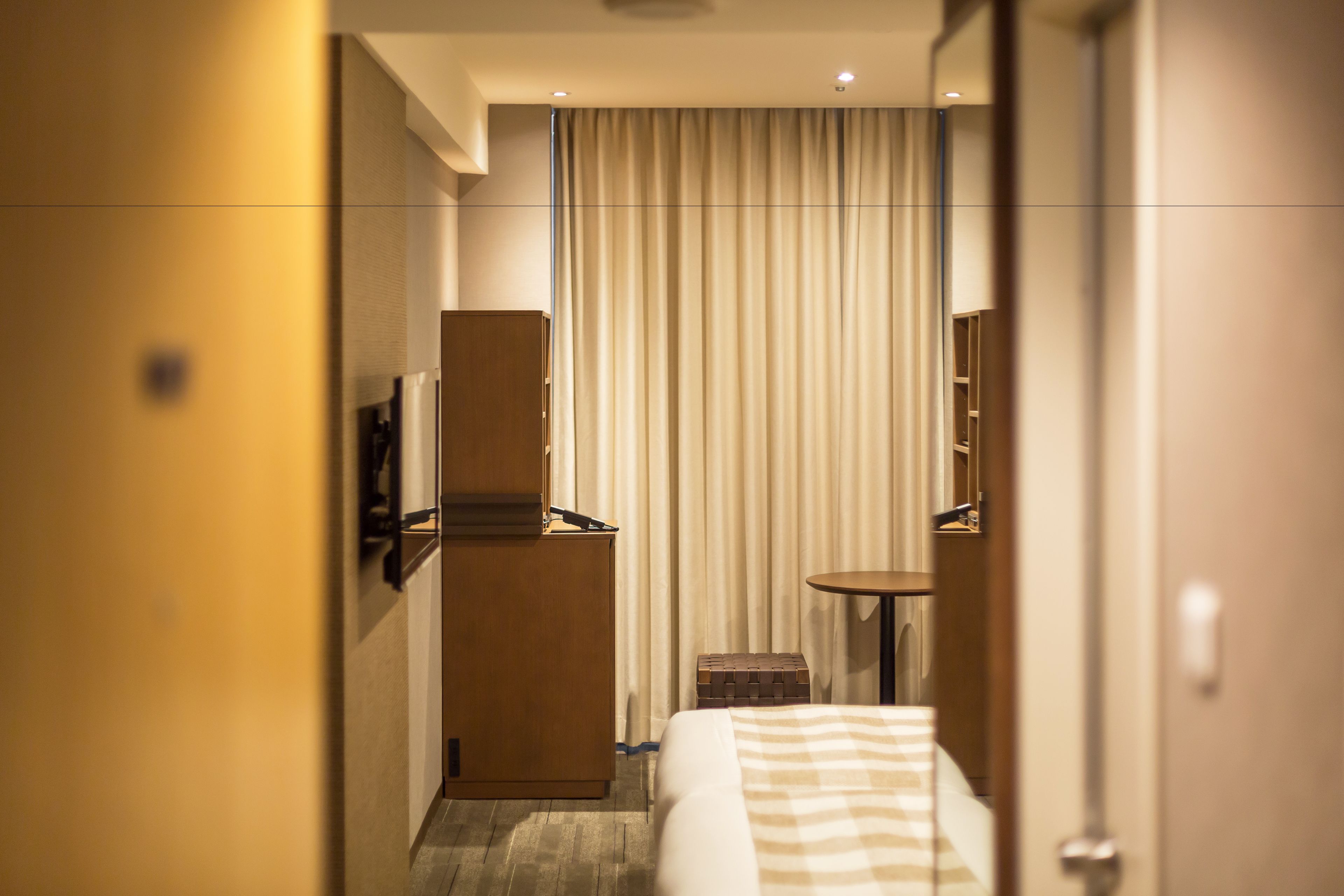 Una habitación de hotel con cama, una mesita, televisor montado en la pared y cortina.