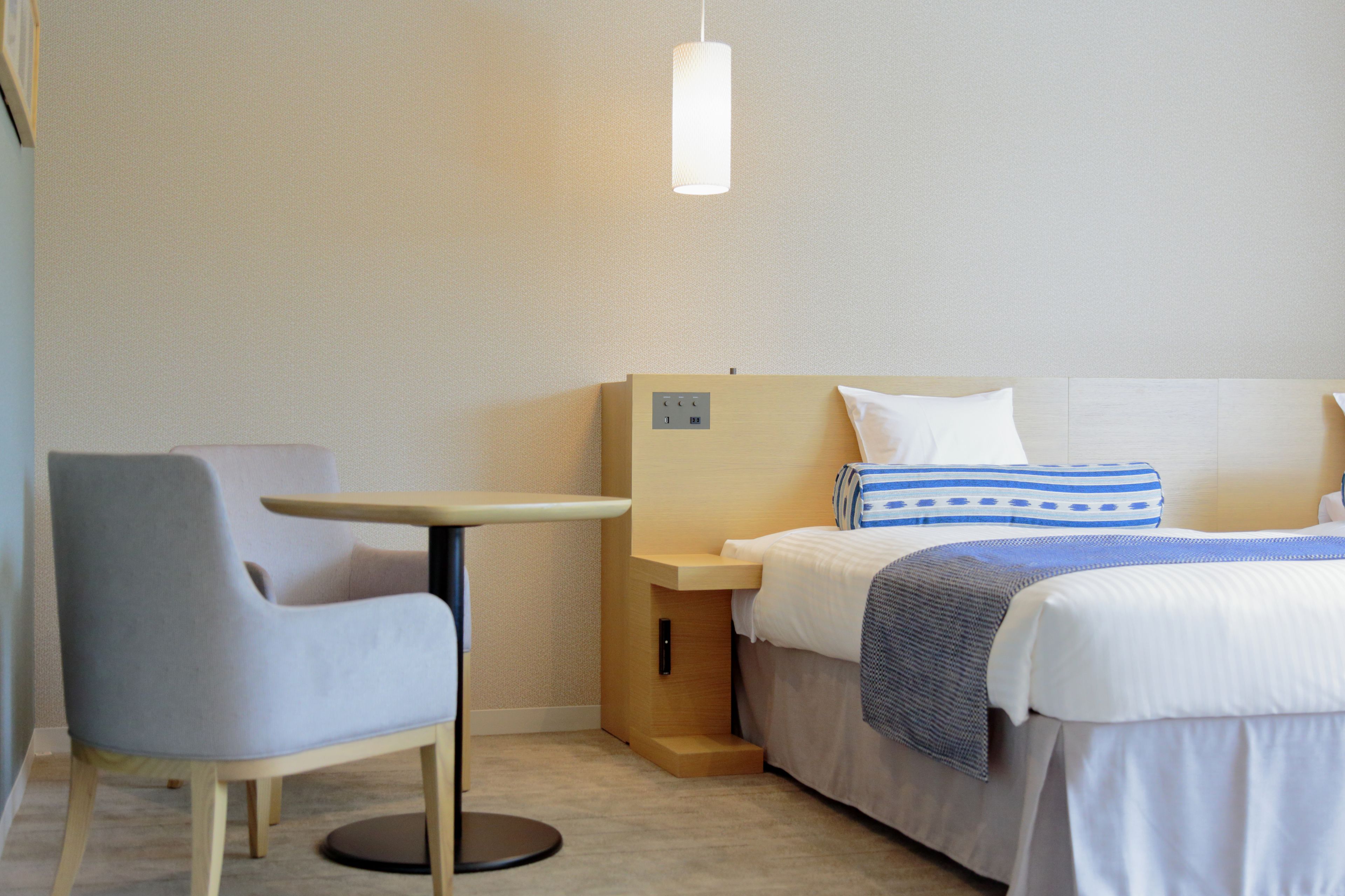 Een hotelkamer met een bed, nachtkastje, stoel en hanglamp.
