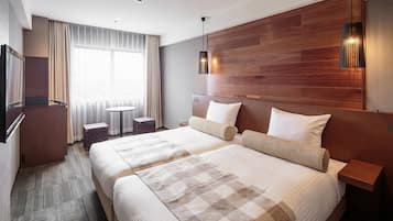 A hotel room with two beds, a wooden headboard, a television, a small table, and a window with curtains.