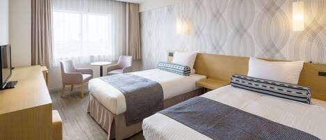 A hotel room with two beds, a desk, a chair, and a large window with curtains.